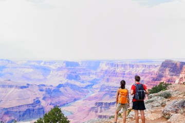two hikers standing on canyon ledge looking out at scenery